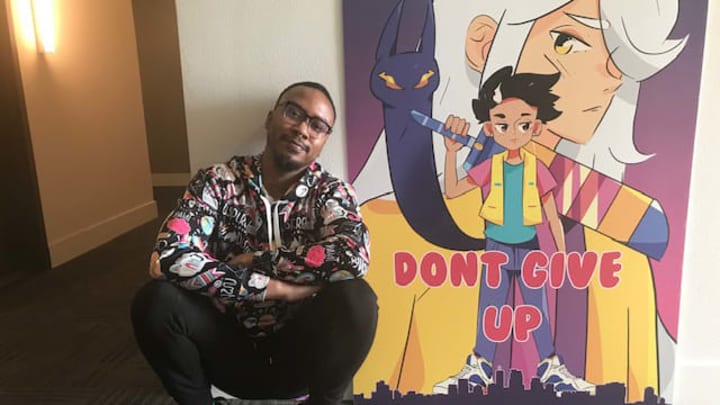 Tristan Barona poses in front of a poster for Don't Give Up: A Cynical Tale.